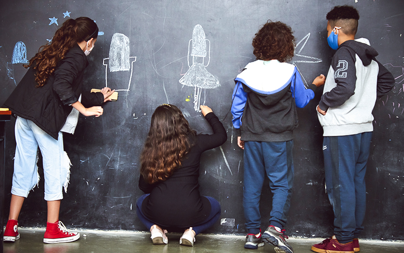 Fotografia de crianças escrevendo com giz no quadro da sala de aula do Alicerce Educação
