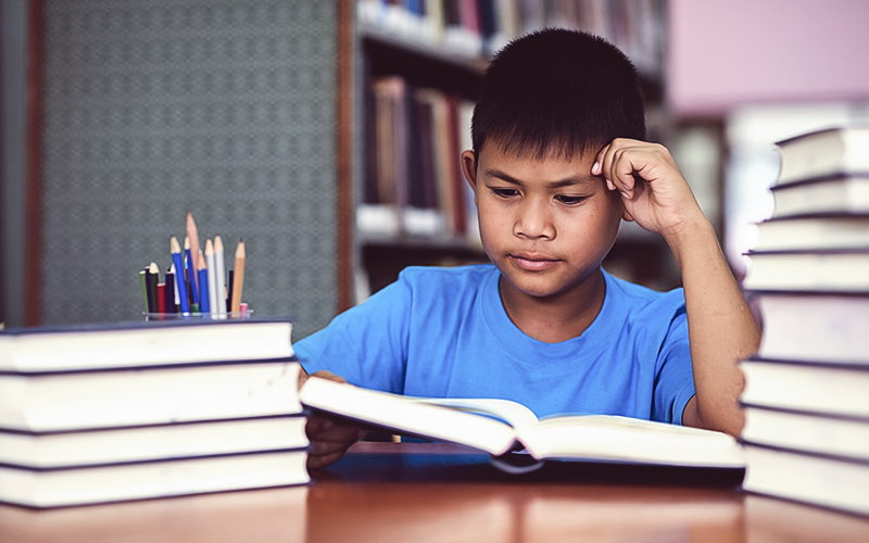 Fotografia de um menino lendo um livro em uma biblioteca