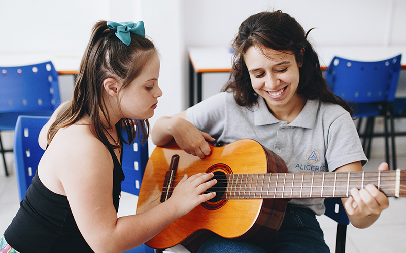 Fotografia de aluna e educadora Alicerce tocando violão na sala de aula