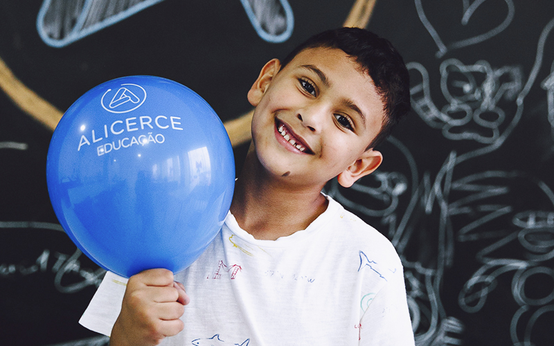 Fotografia de aluno Alicerce sorrindo e segurando um balão do Alicerce