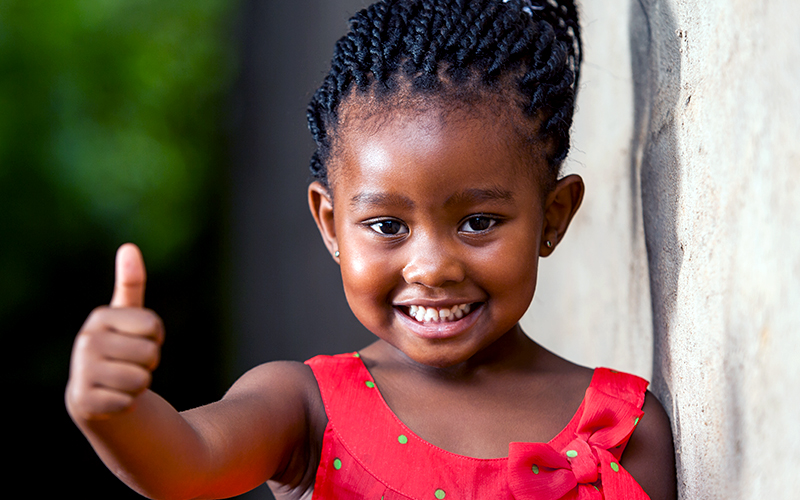 Foto de uma criança feliz fazendo um sinal de positivo com as mãos